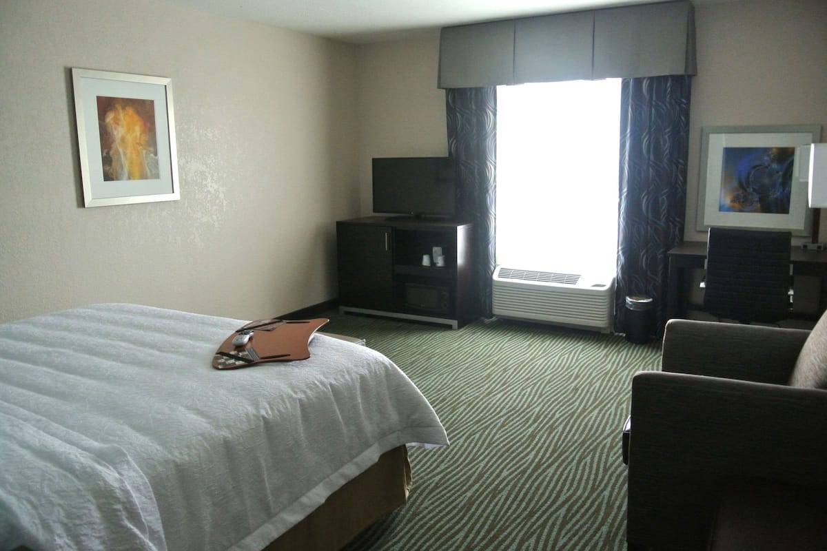 A hotel room with a bed, a desk, a chair, a television, and a window with curtains.