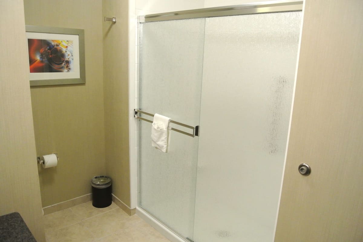 A bathroom with a glass shower door, a towel rack, a trash can, and a framed picture on the wall.