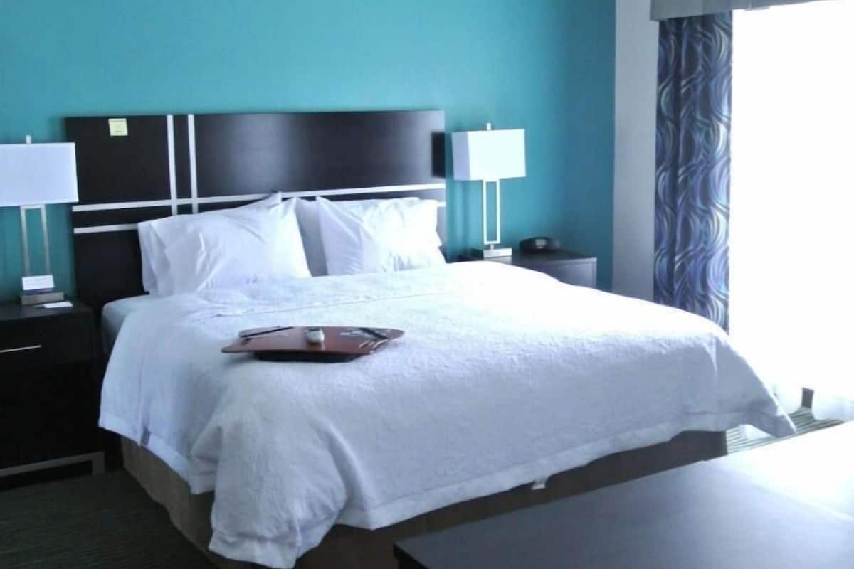 A hotel room with a bed, nightstands, a desk, and a lamp.