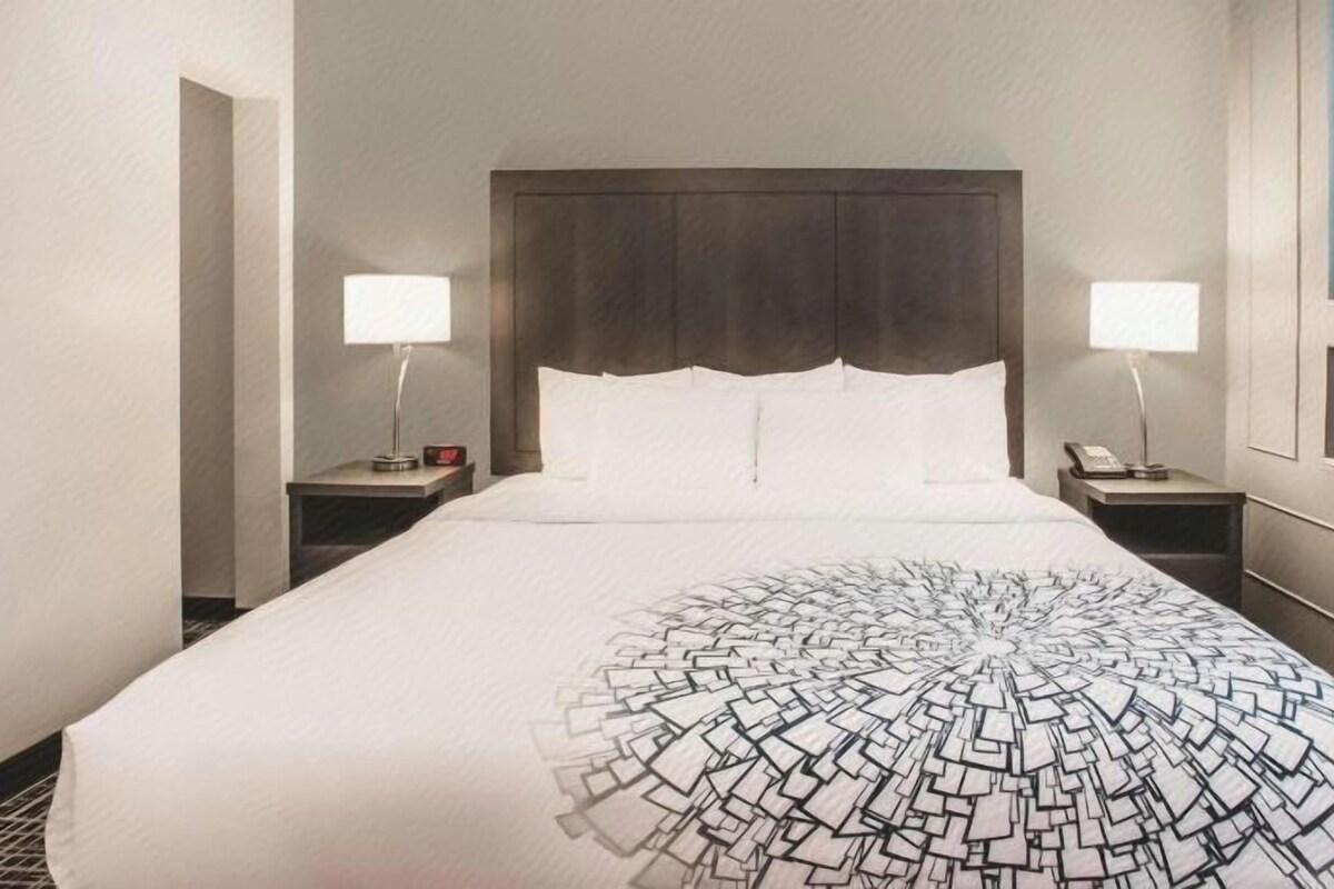 Habitación de hotel con una cama grande, dos mesitas de noche, un cabecero y una lámpara fijada a la pared.