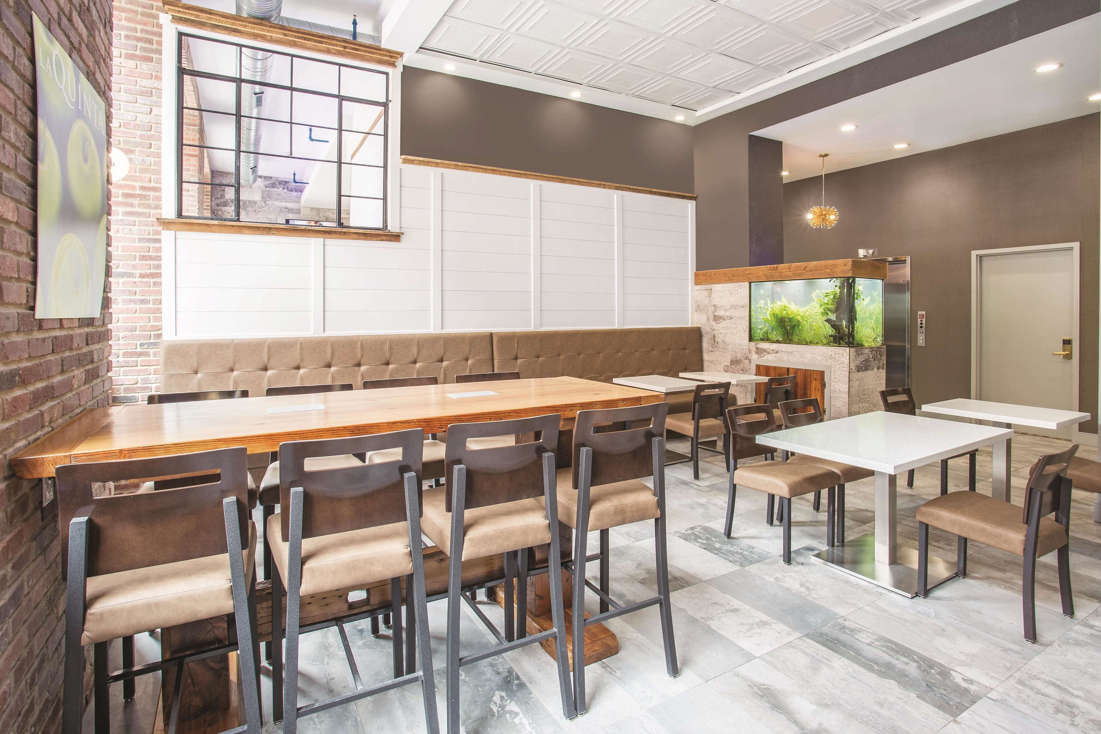 A restaurant with a long wooden table, cushioned chairs, a brick wall, and a large aquarium.