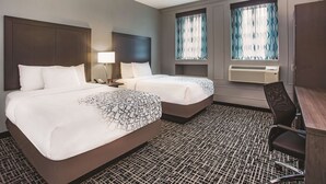 A hotel room with two beds, a desk, a chair, and a window with patterned curtains. - La Quinta Inn & Suites by Wyndham Baltimore Downtown (Baltimore)