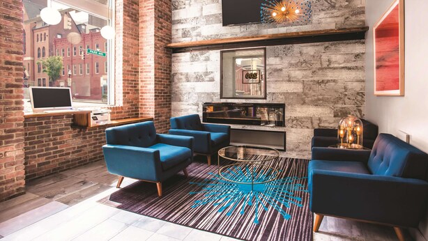 A modern lounge with brick walls, a large window, and blue seating. - La Quinta Inn & Suites by Wyndham Baltimore Downtown (Baltimore)