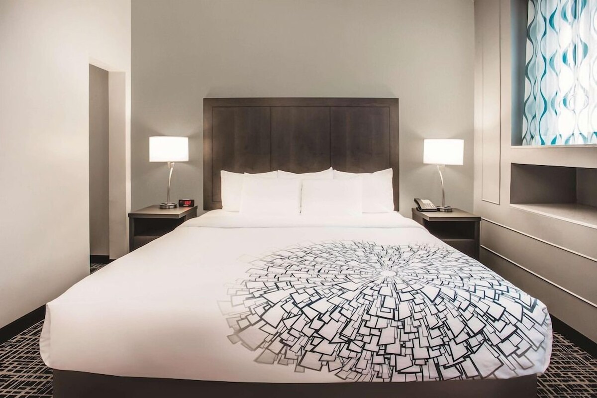 Una habitación de hotel con una cama grande, dos mesitas de noche y un cabecero.