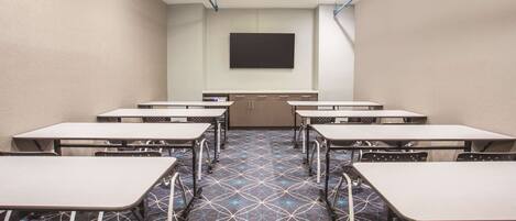 A conference room with tables and chairs, a flat-screen TV, and a patterned carpet.