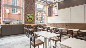 A restaurant interior with brick walls, large windows, and a mix of seating options including tables and a cushioned bench area. - La Quinta Inn & Suites by Wyndham Baltimore Downtown (Baltimore)