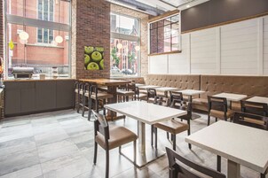 Interior de un restaurante con paredes de ladrillo, ventanas amplias y una variedad de opciones de asientos, incluyendo mesas y un área con bancos acolchados.