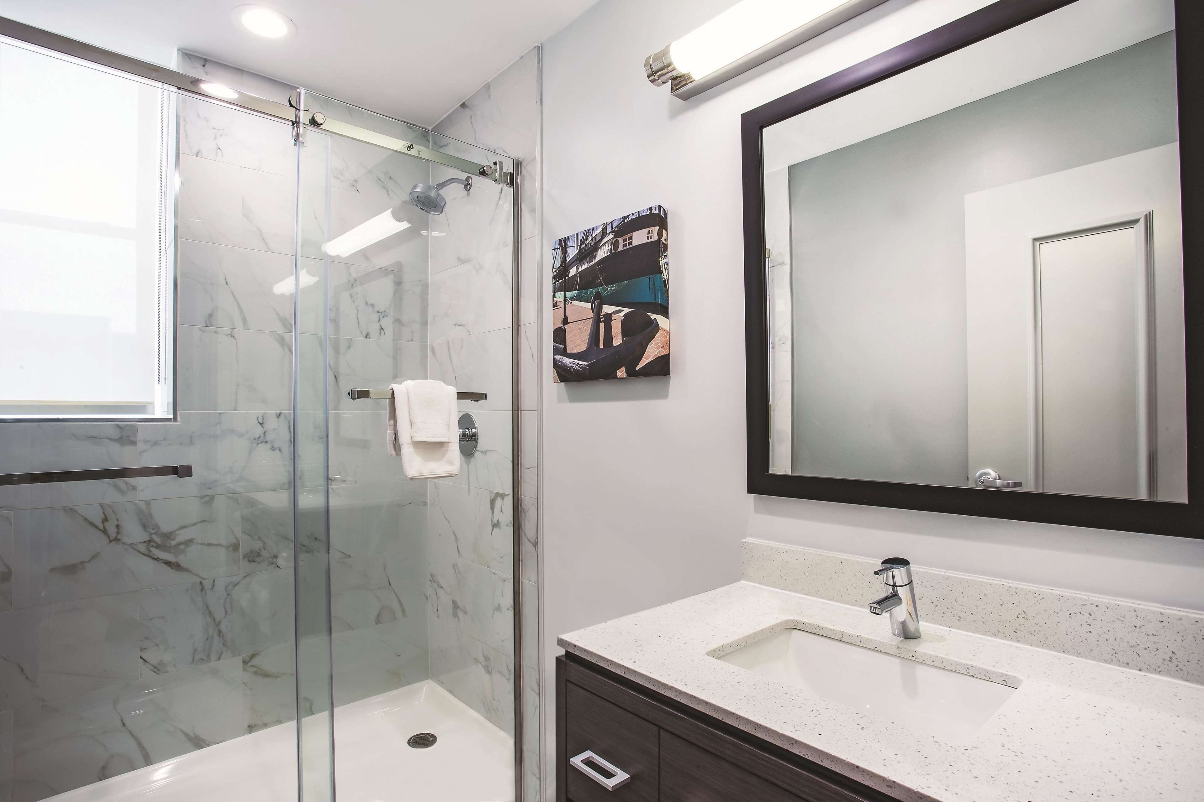 A modern bathroom with a glass-enclosed shower, a large mirror, and a white sink.