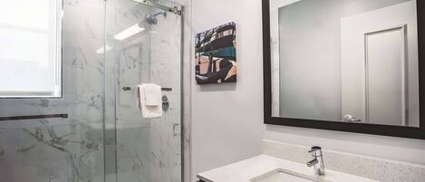 A modern bathroom with a glass-enclosed shower, a large mirror, and a white sink.