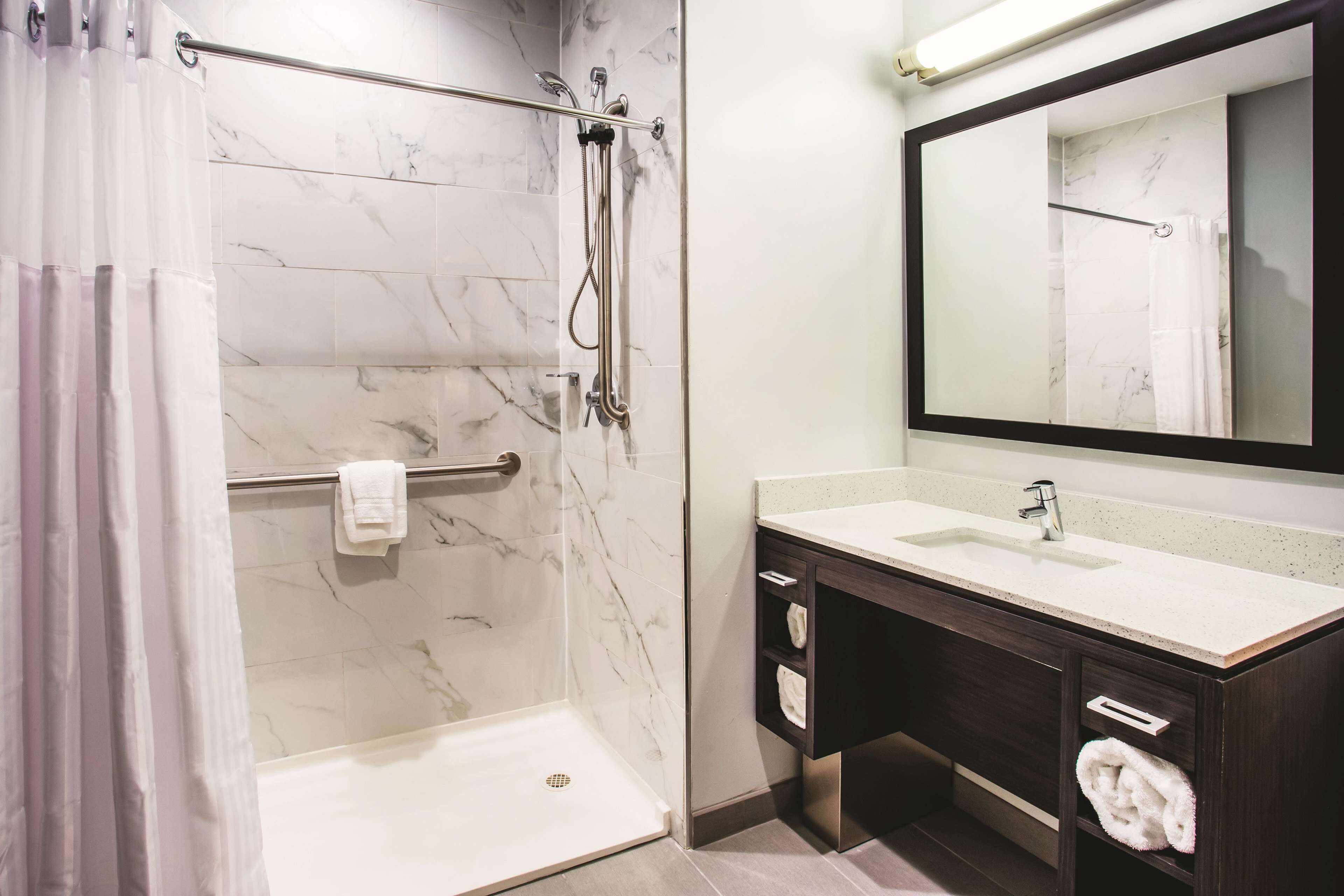 Uma casa de banho moderna com cabine de duche, um espelho grande e toucador com lavatório e porta-toalhas.