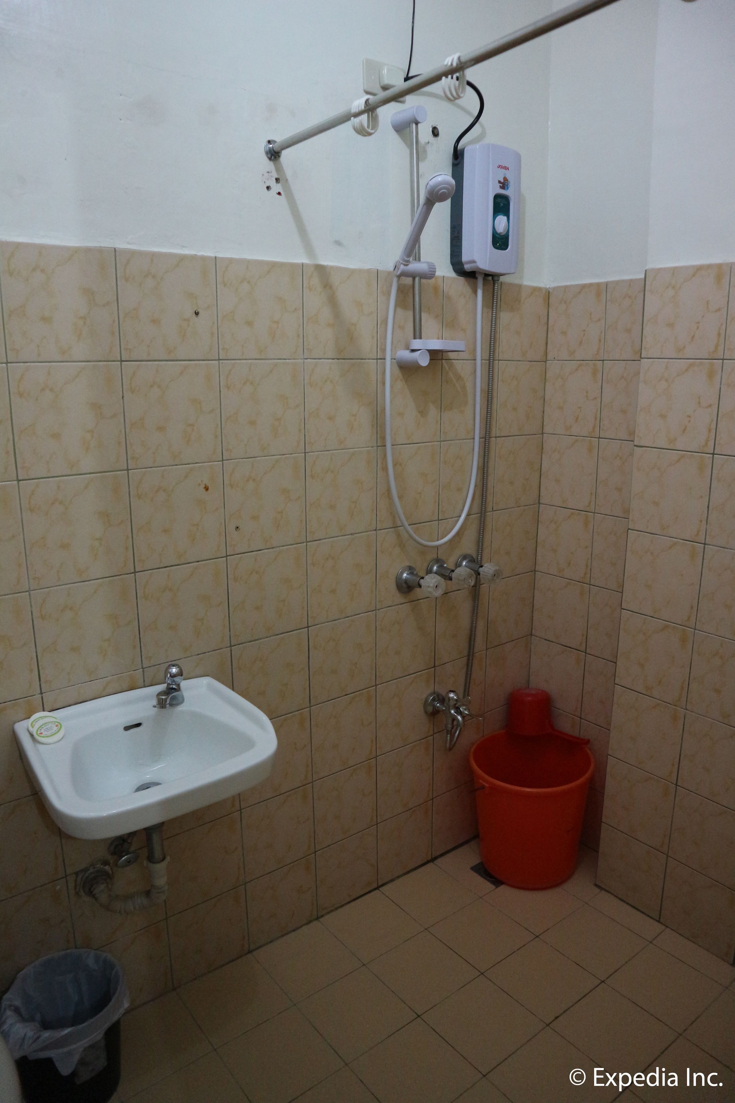 A bathroom with a sink, a handheld showerhead, and a red bucket.
