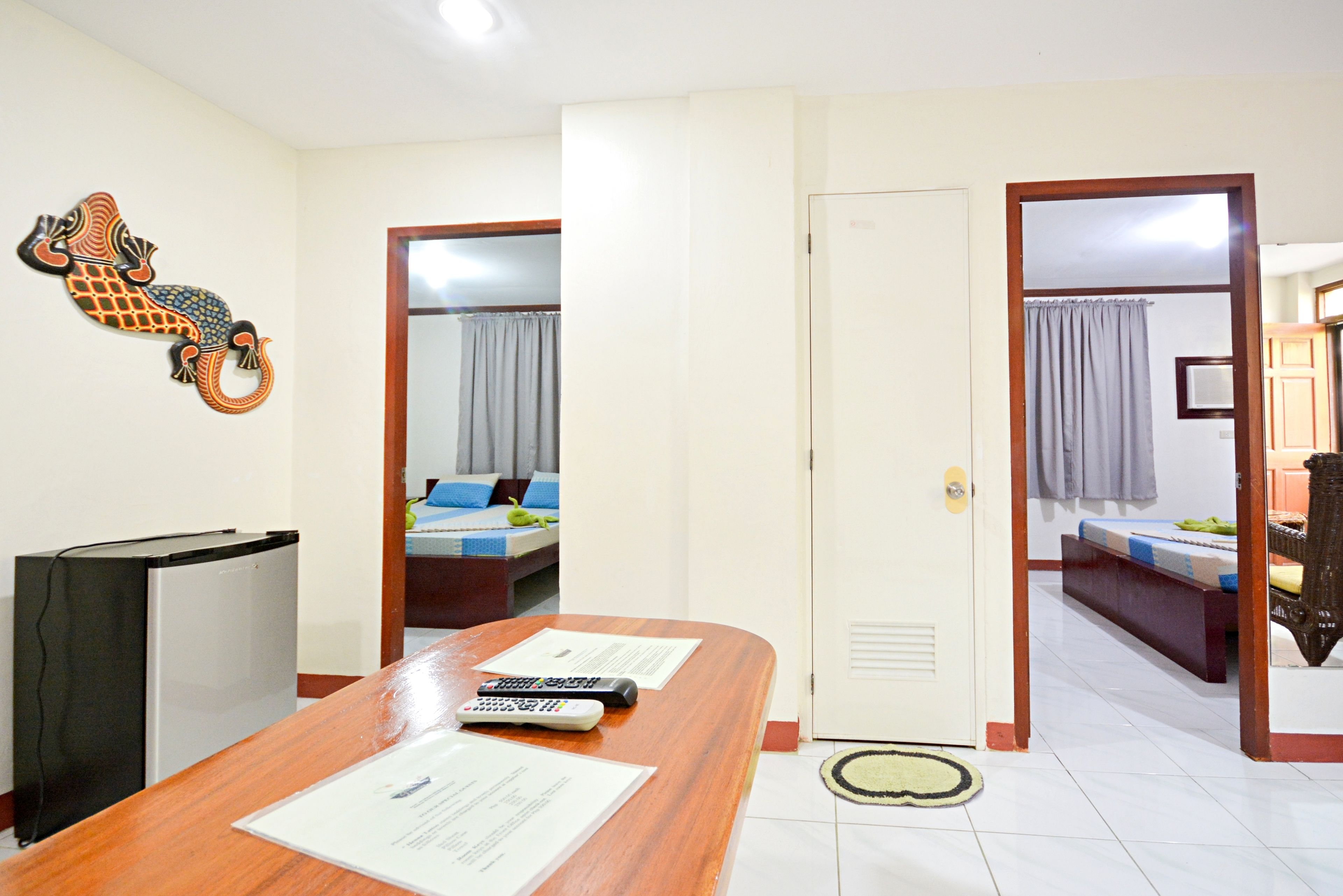 A hotel room with a wooden desk, a refrigerator, a bed with a blue and white bedspread, and a bathroom visible through an open door.