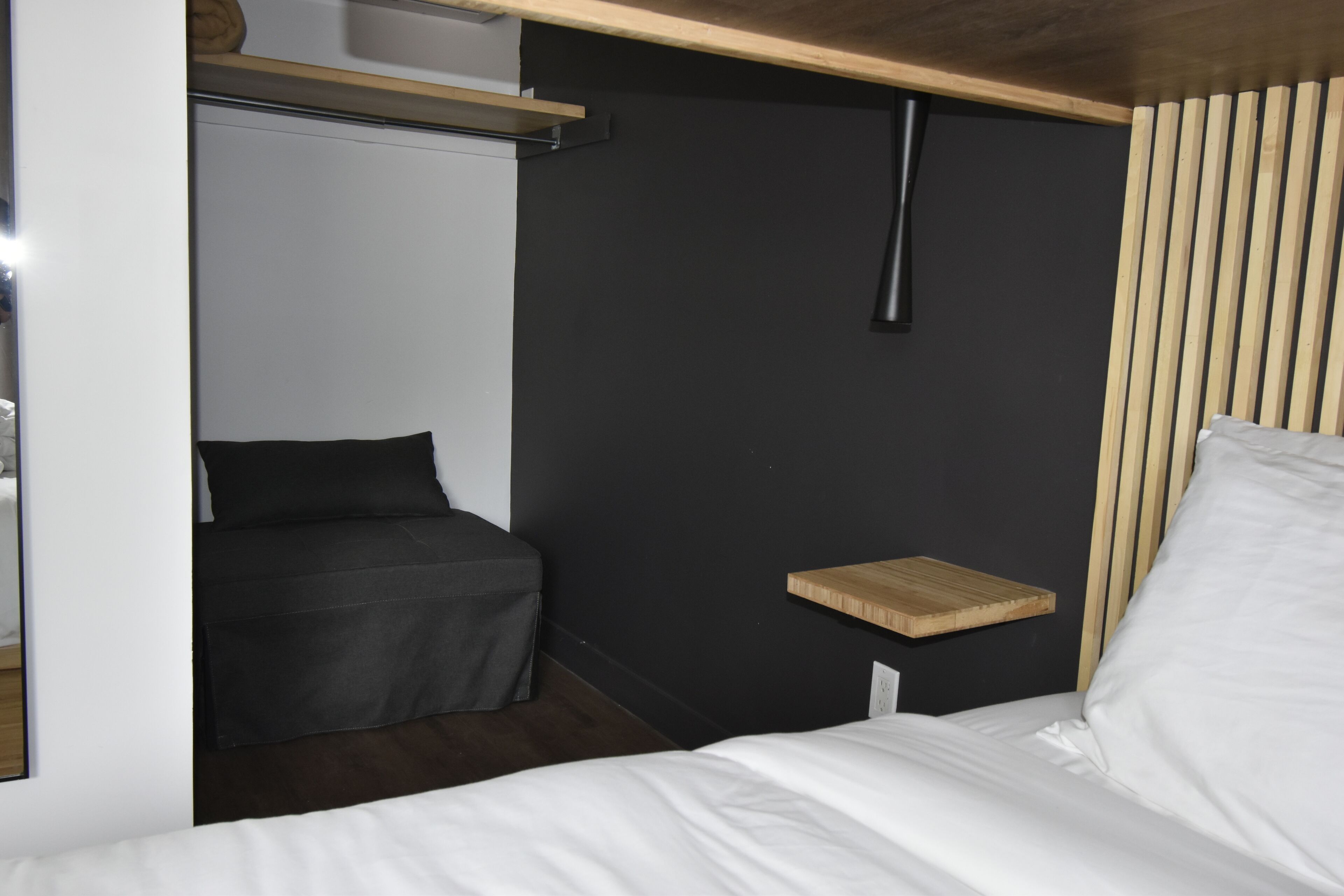 A compact room with a bed, a small seating area, and a shelf.