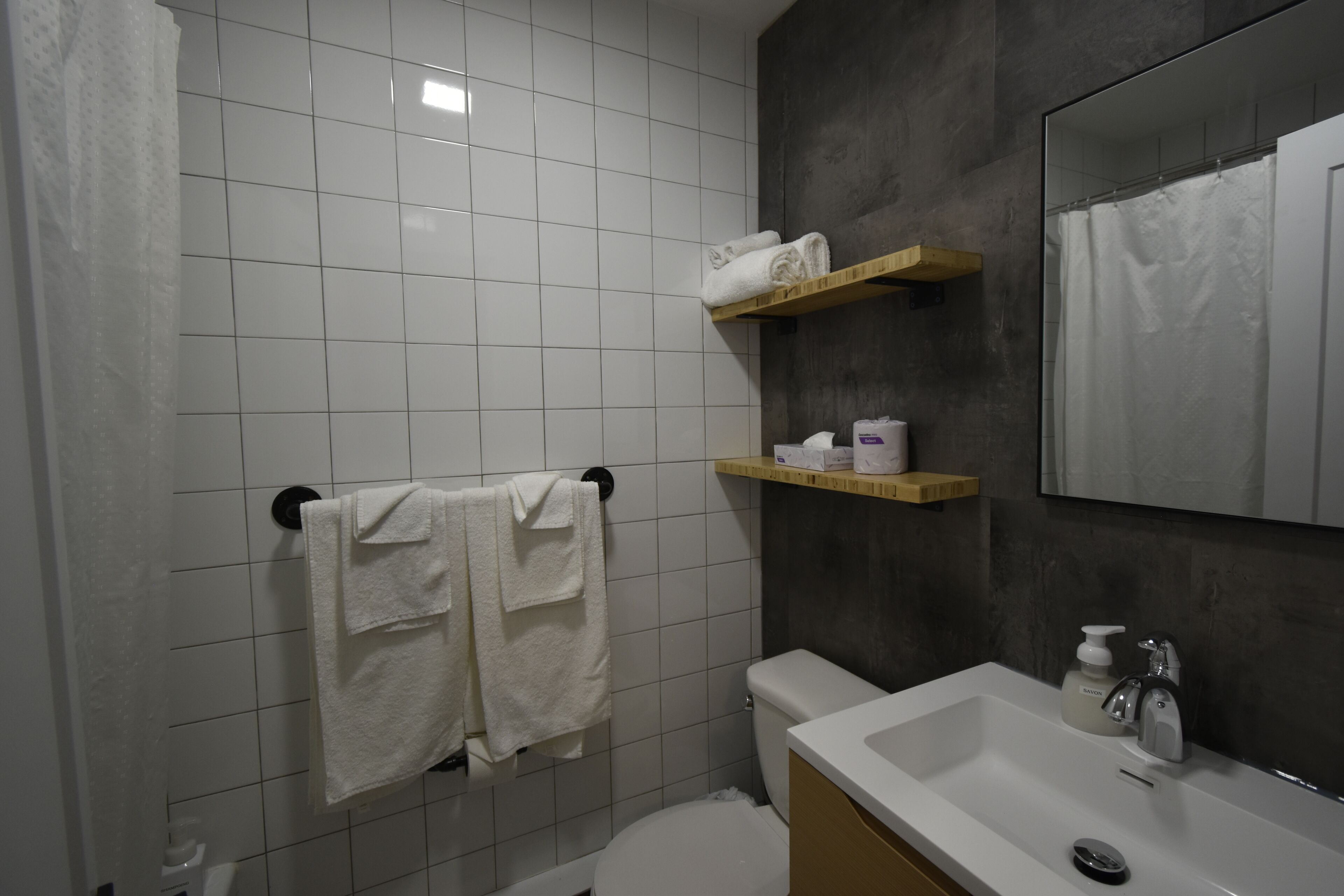 A bathroom with white tiled walls, a toilet, a sink with a mirror, and two towel racks with towels.