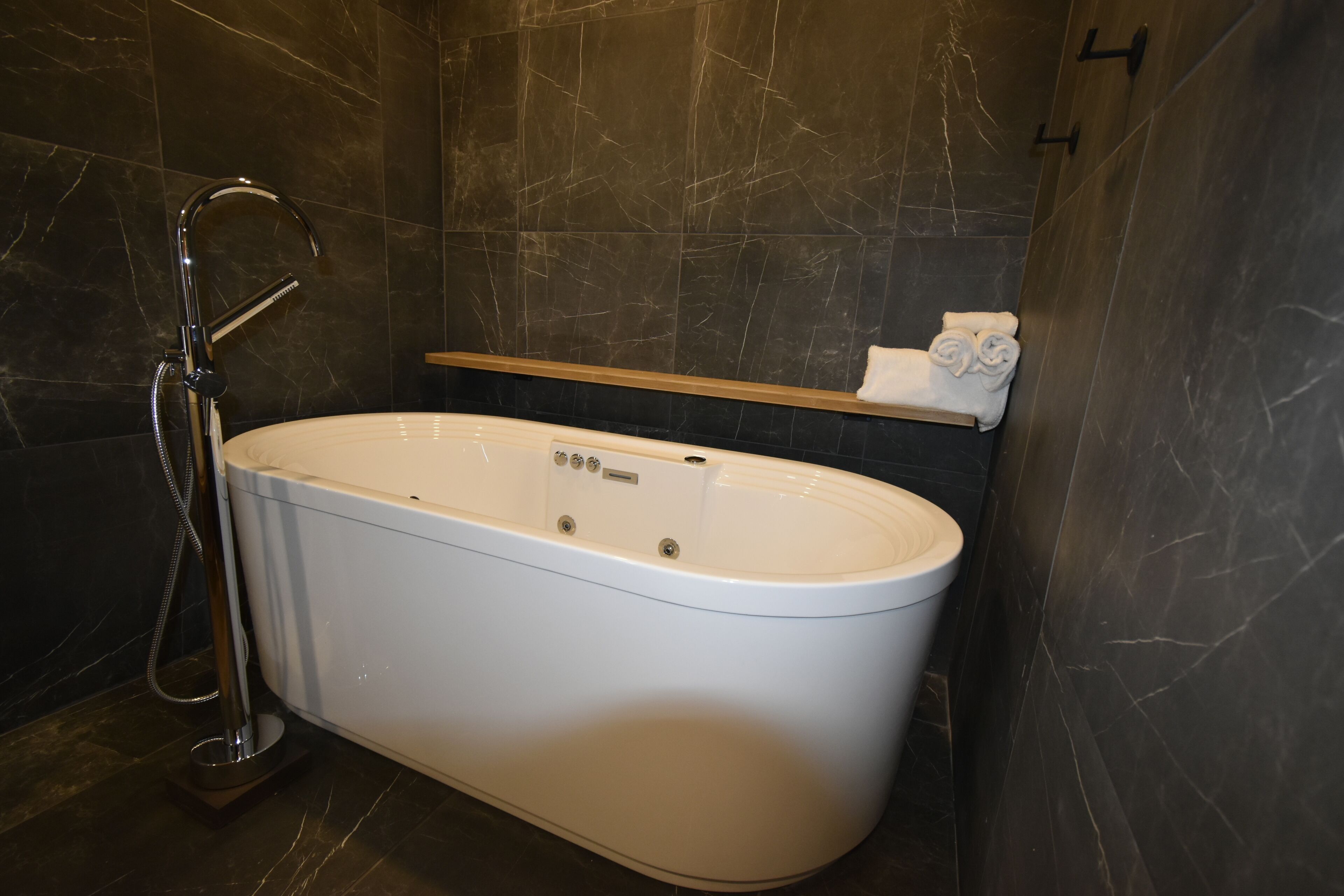 Un baño moderno con una bañera independiente, un cabezal de ducha de mano y un perchero para toallas.