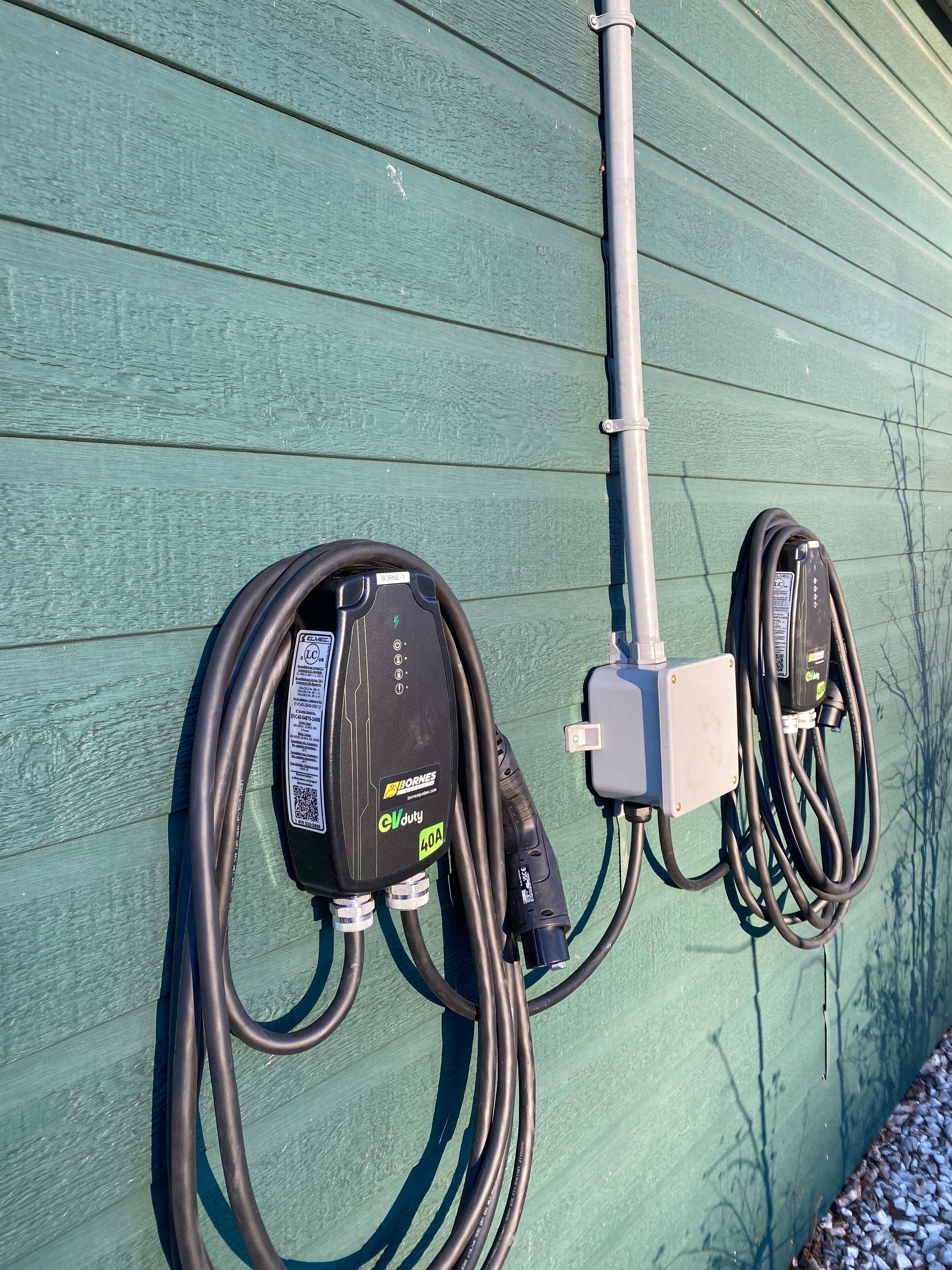 A green exterior wall with two electrical boxes and two power cords.