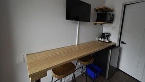 Een kitchenette met een houten aanrecht, een magnetron, een koelkast en een aan de muur bevestigde televisie.