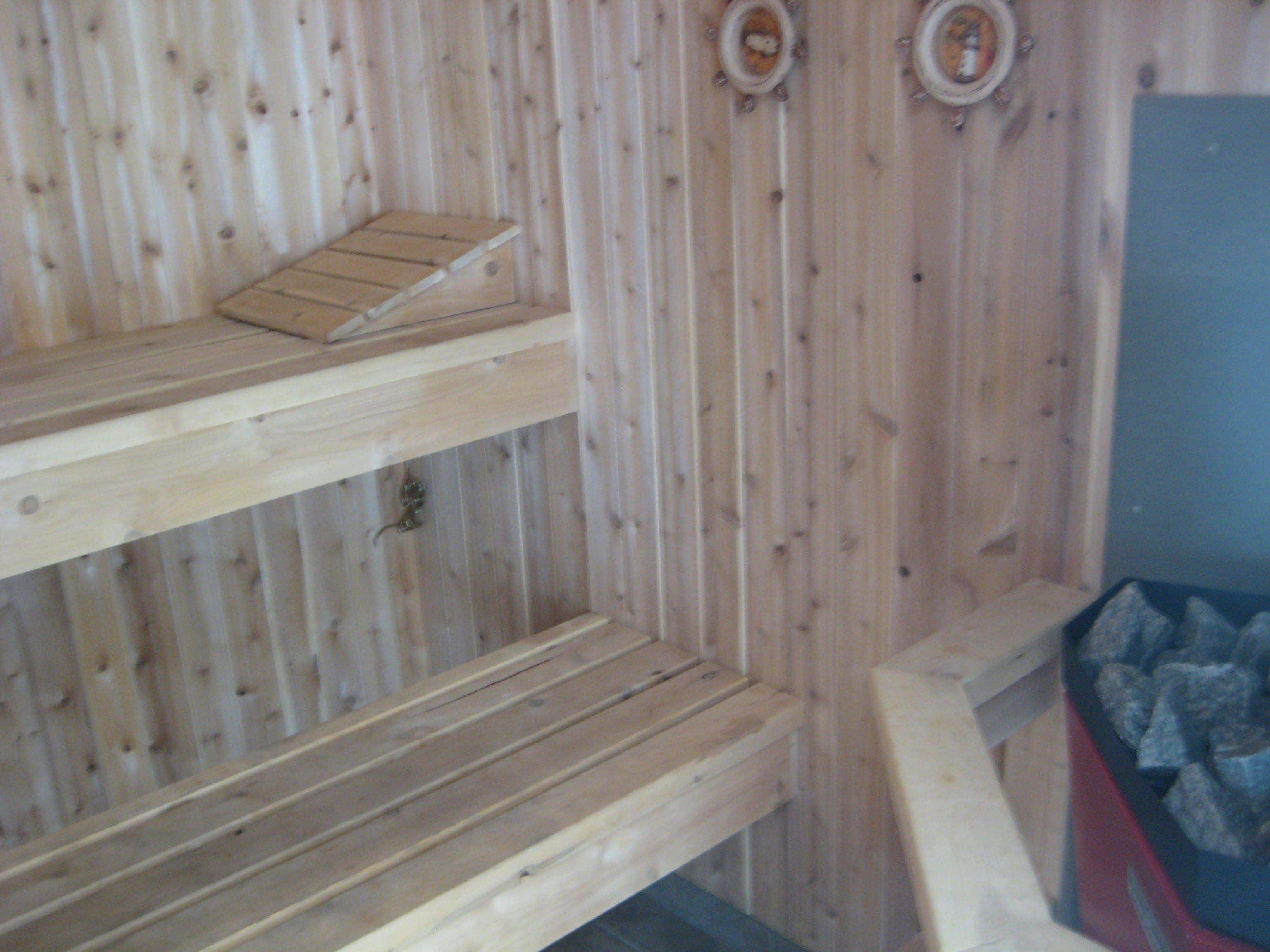 A wooden sauna with multiple benches and a blue container with stones.