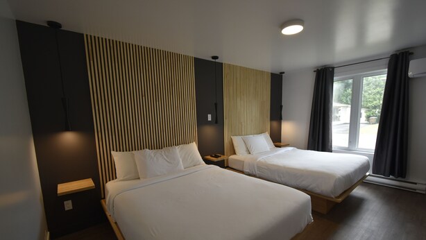 Een hotelkamer met twee bedden, een houten nachtkastje, een wandlamp en een groot raam met gordijnen.