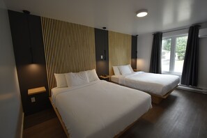 A hotel room with two beds, a wooden nightstand, a wall-mounted lamp, and a large window with curtains. - Motel ANF (Drummondville)