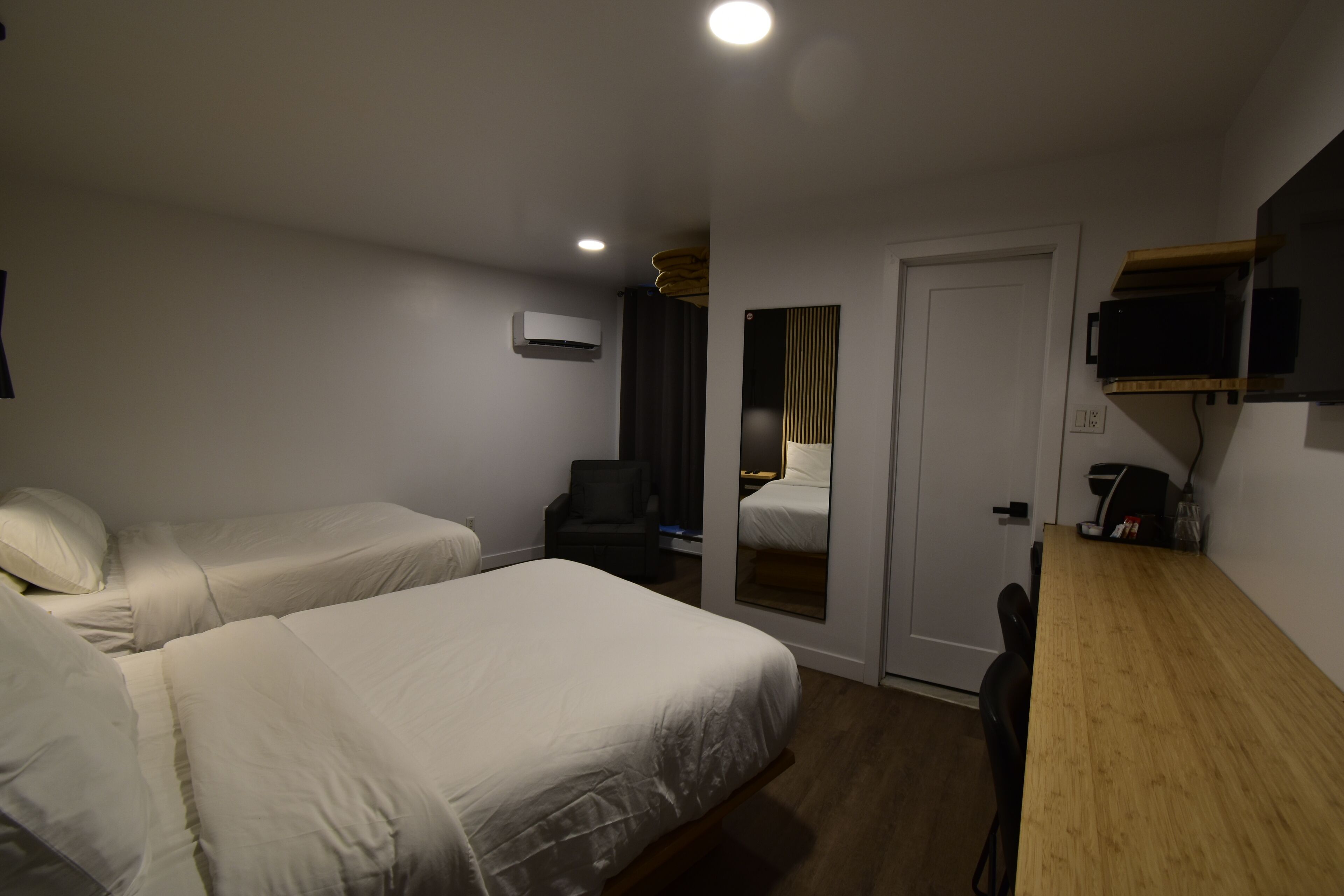 A hotel room with two beds, a desk, a chair, a TV, and a mirror.