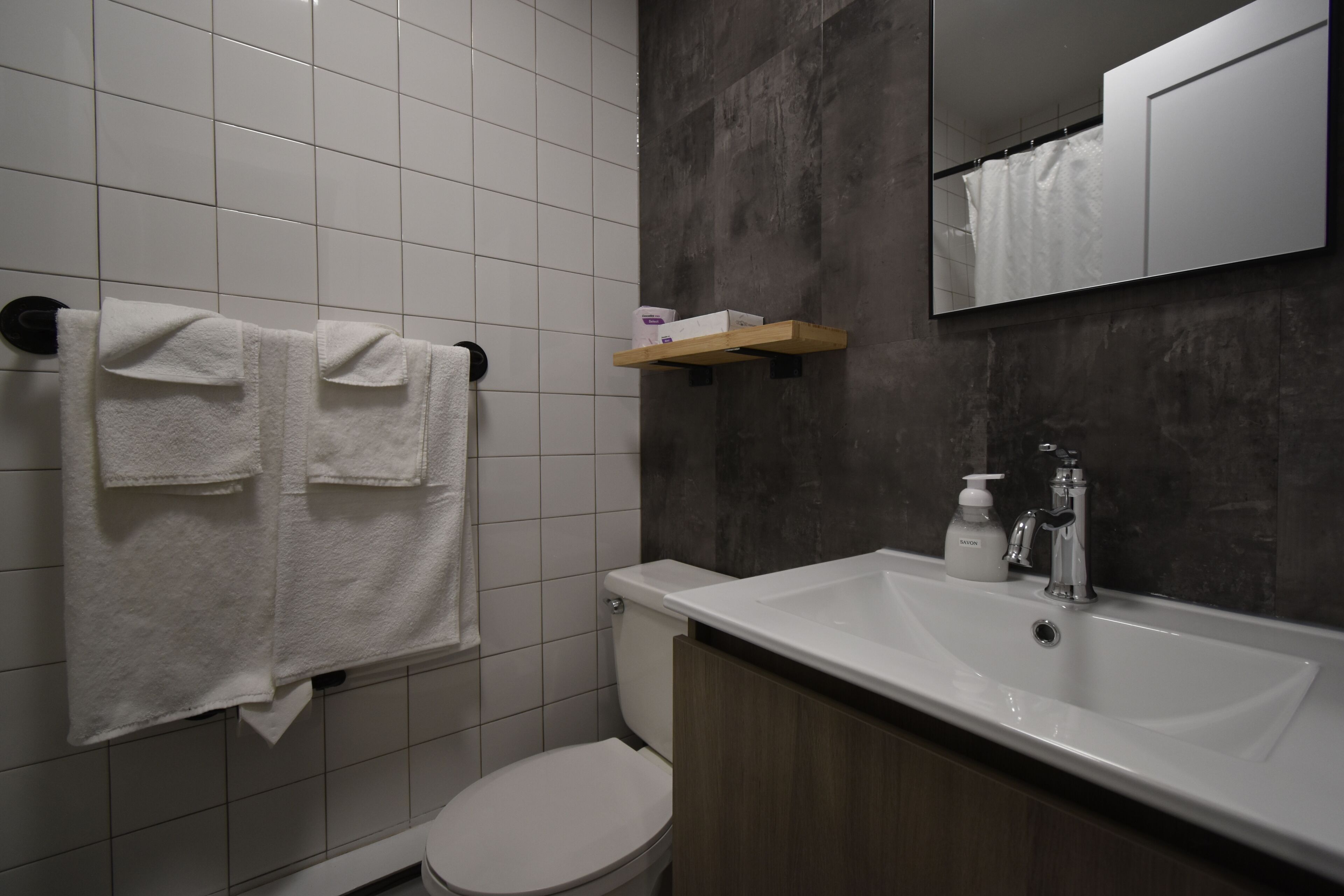 A bathroom with a toilet, a sink, and a mirror. There are two towels hanging on a rack.