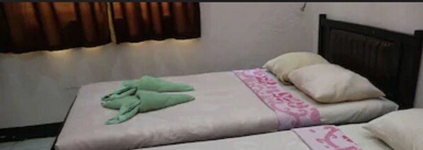 Una cama individual con colchón blanco, pantuflas verdes y una colcha estampada en rosa y blanco.