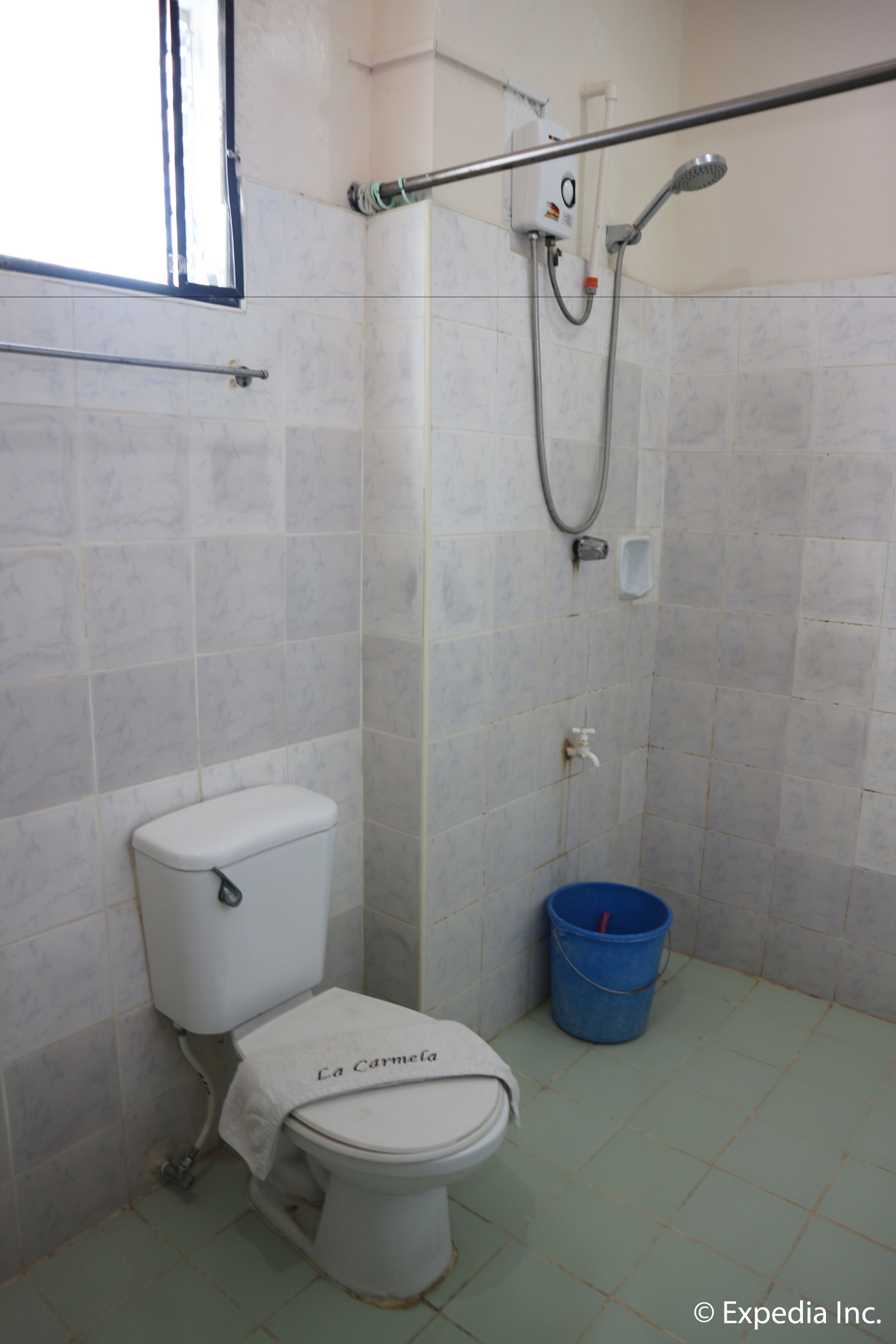 A small bathroom with a toilet, a shower, and a blue bucket.