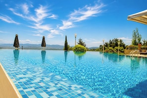 Une piscine d’un bleu éclatant, avec un revêtement de carrelage, entourée de verdure et surplombée d’un ciel dégagé.