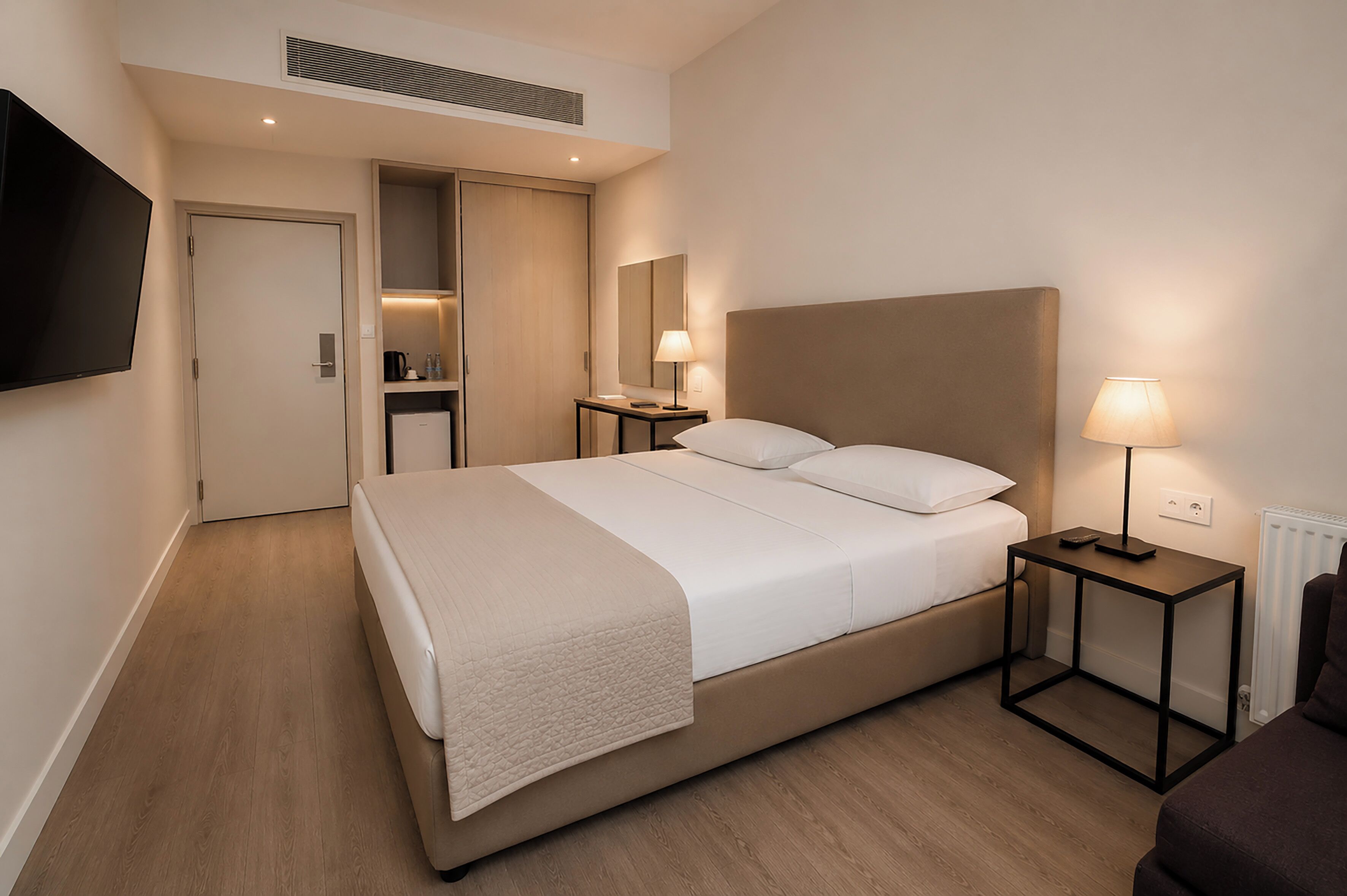Ein modernes Hotelzimmer mit einem großen Bett, Nachttischen, einem Fernseher und einem Spiegel.