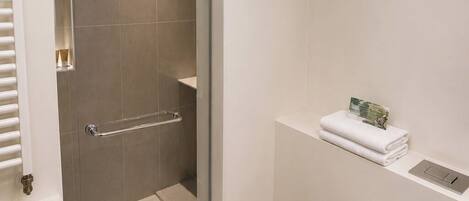 A modern bathroom with a glass-enclosed shower, a white toilet, and a small shelf with towels.