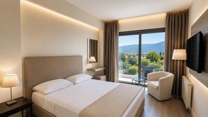 A hotel room with a bed, a chair, a TV, a window with a view, and a lamp. - Droushia Heights (Droushia)