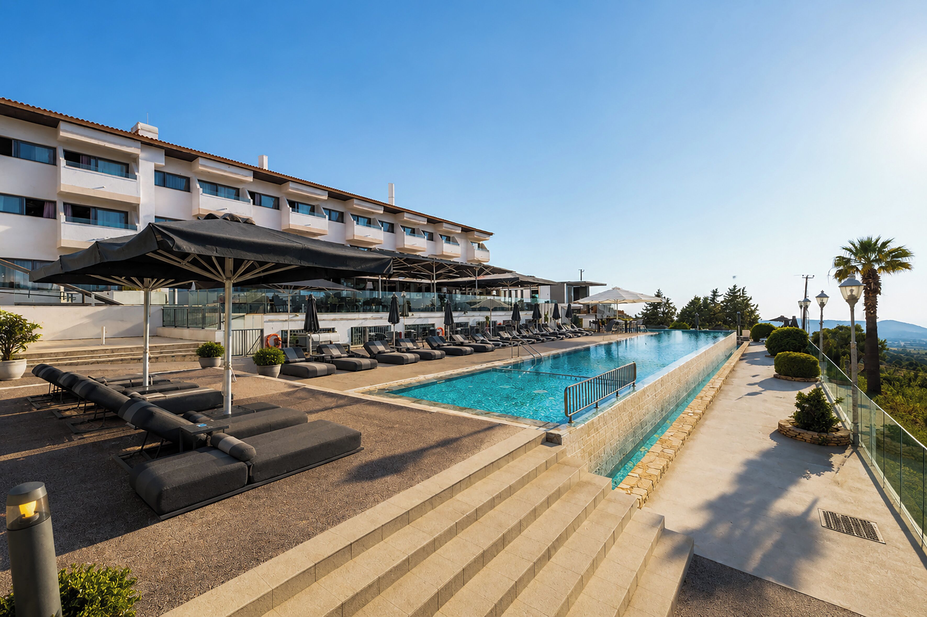 A hotel with a swimming pool, sun loungers, and a view of the mountains.