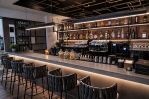 Un espace bar doté d’un long comptoir, de plusieurs étagères remplies de bouteilles et de plusieurs tabourets de bar noirs.