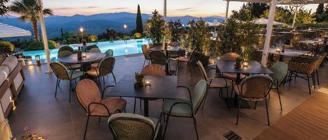 An outdoor patio with tables and chairs, a pool, and a view of mountains.