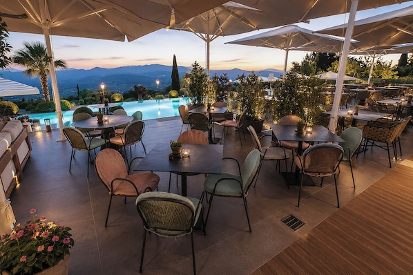 Une terrasse extérieure avec des tables et des chaises, une piscine et une vue sur les montagnes.