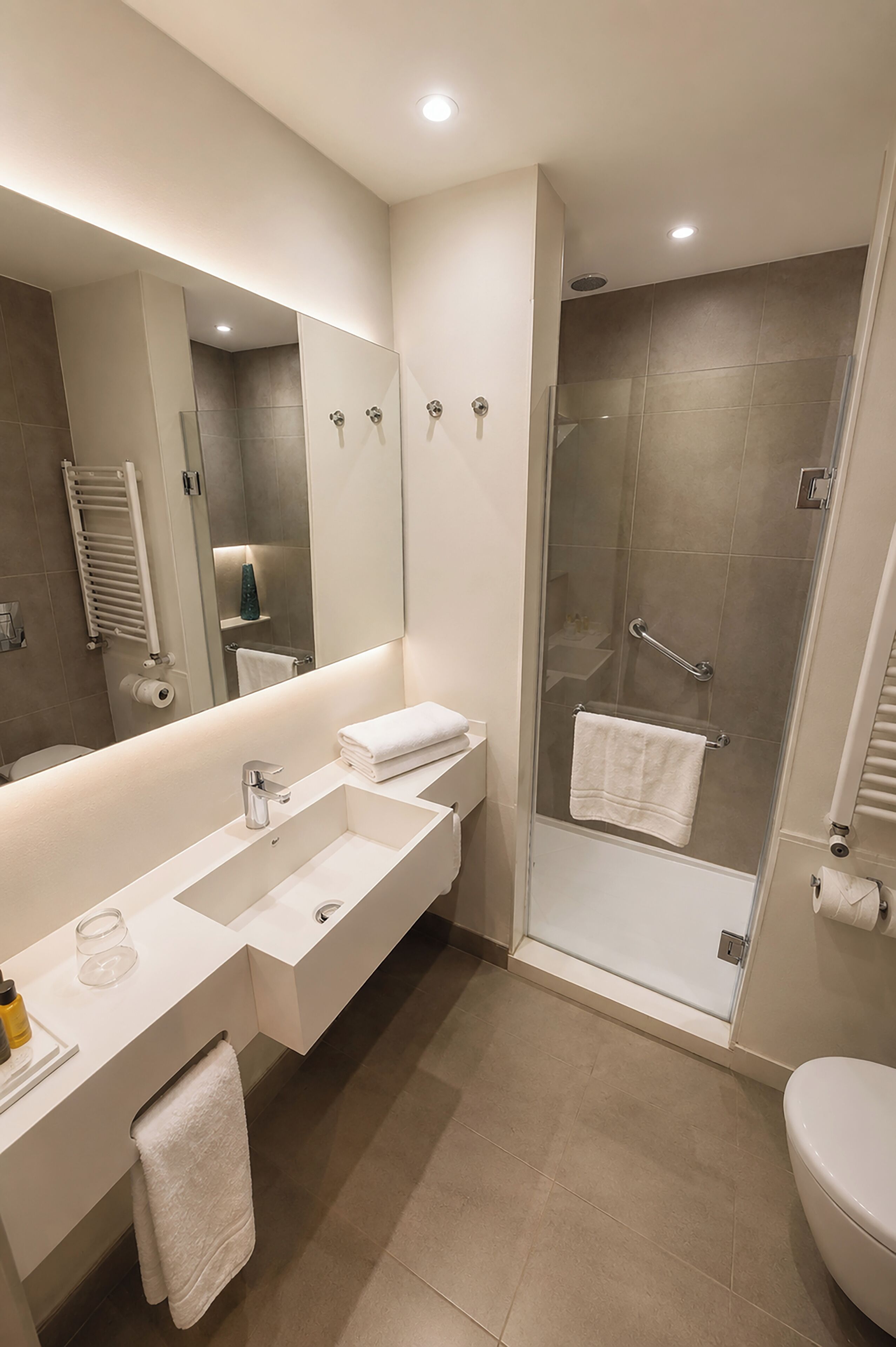 Un baño moderno con un espejo grande, cabina de ducha, lavamanos y retrete.