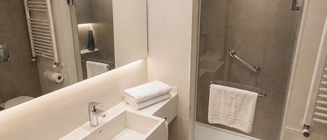 Un baño moderno con un espejo grande, cabina de ducha, lavamanos y retrete.
