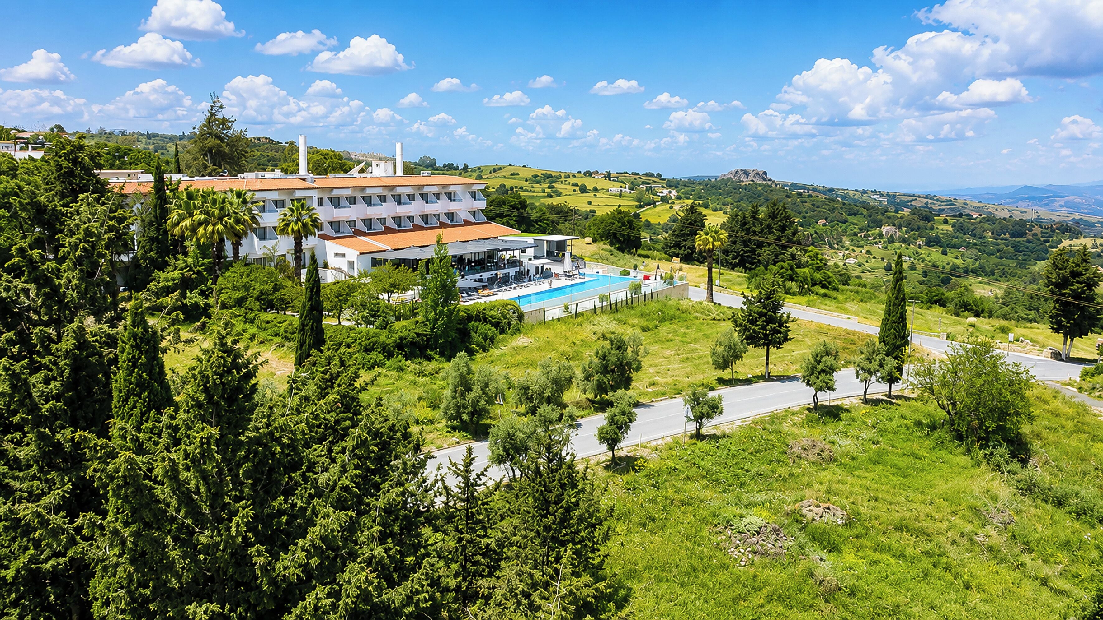 Un hotel con piscina, rodeado de vegetación y colinas.