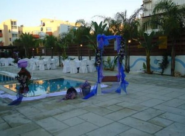 An outdoor area with a pool, white chairs, and a blue decorative structure. - Valana Hotel Apartments (Limassol)