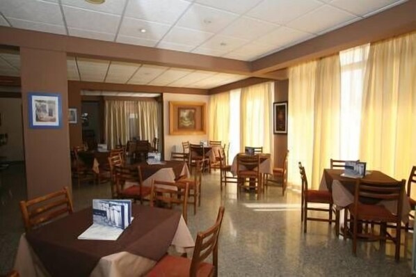 A hotel dining area with multiple tables and chairs, a ceiling with recessed lighting, and large windows with curtains. - Valana Hotel Apartments (Limassol)