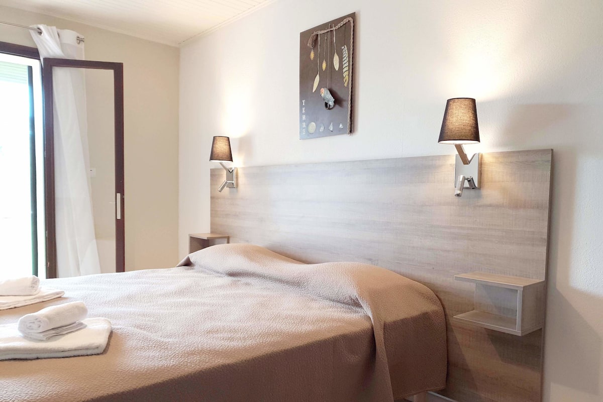 Habitación de hotel con cama, dos lámparas de pared, cabecera de madera y mesita de noche pequeña.
