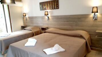Habitación de hotel con dos camas, cada una con una colcha color beige y una toalla enrollada. Hay lámparas fijadas a la pared y una pieza decorativa sobre las camas.