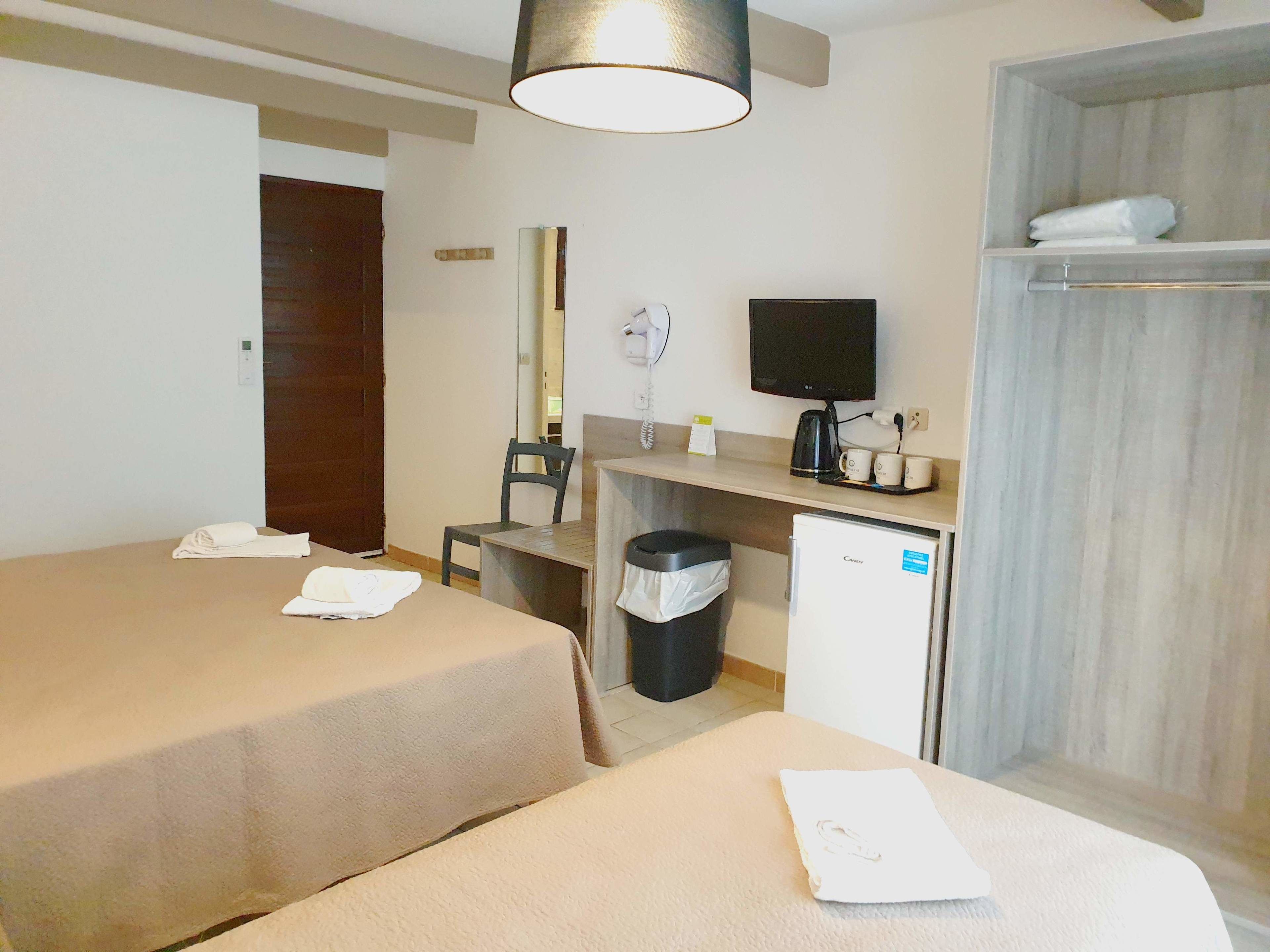 A hotel room with two beds, a desk, a television, a small refrigerator, and a trash bin.