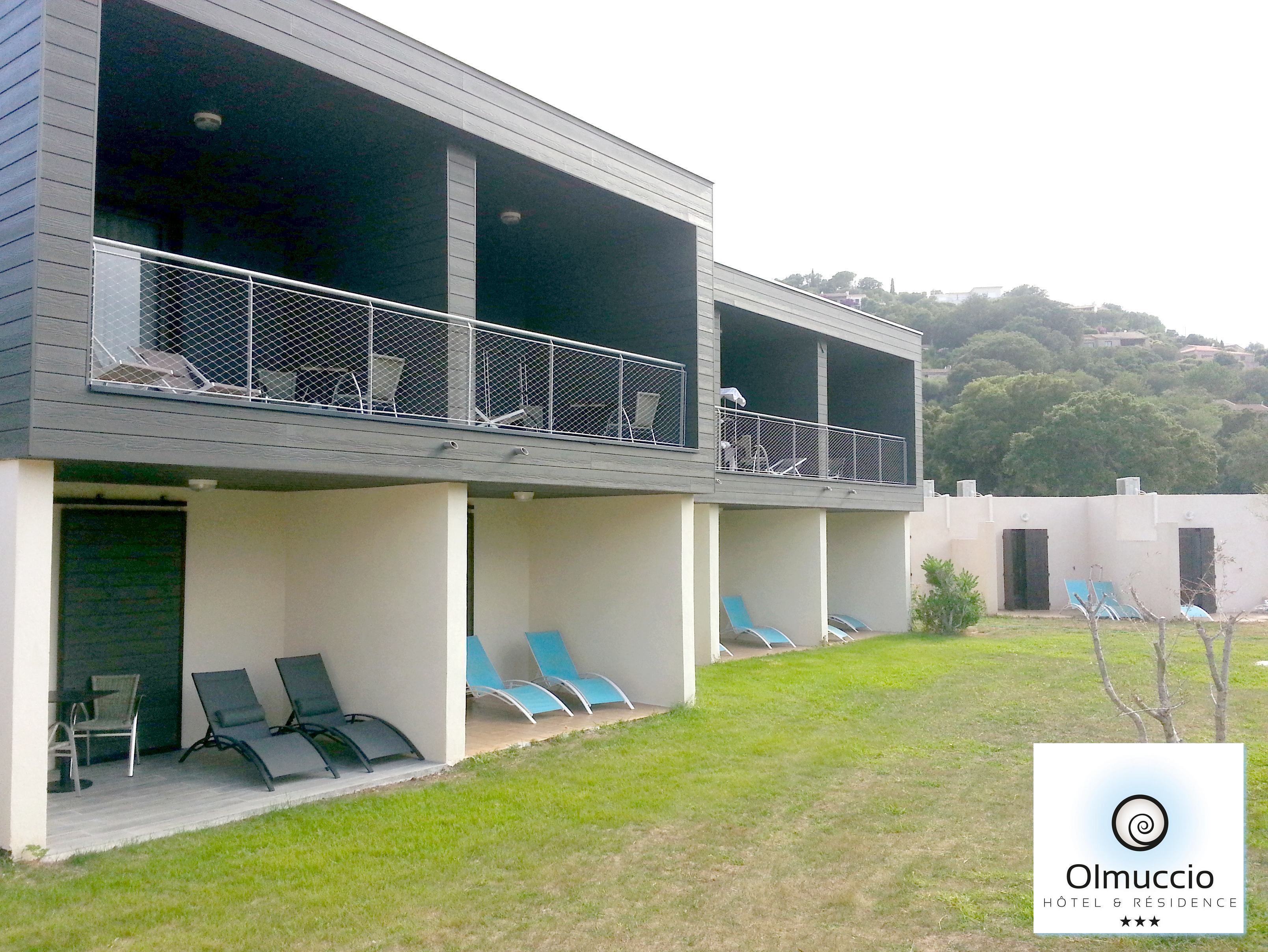 Um hotel moderno com estrutura em dois andares, área externa com espreguiçadeiras e vista para uma paisagem montanhosa.