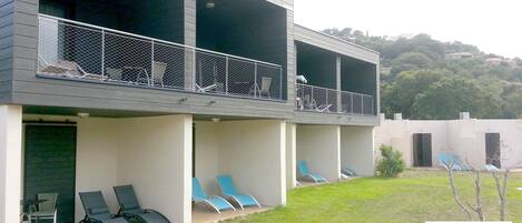 Um hotel moderno com estrutura em dois andares, área externa com espreguiçadeiras e vista para uma paisagem montanhosa.