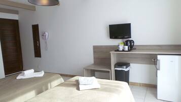 A hotel room with two beds, a desk with a television, a coffee maker, and a trash bin.