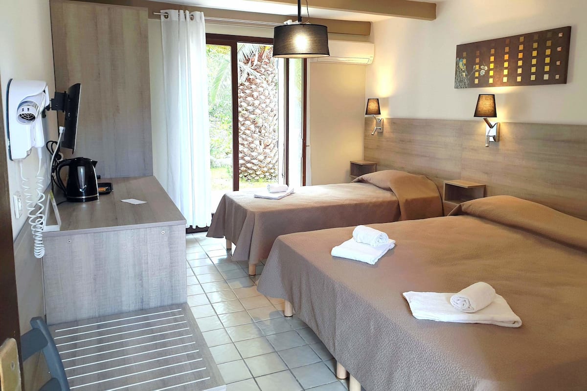 Habitación de hotel con dos camas, un escritorio con secador de pelo y hervidor, y vista al exterior.
