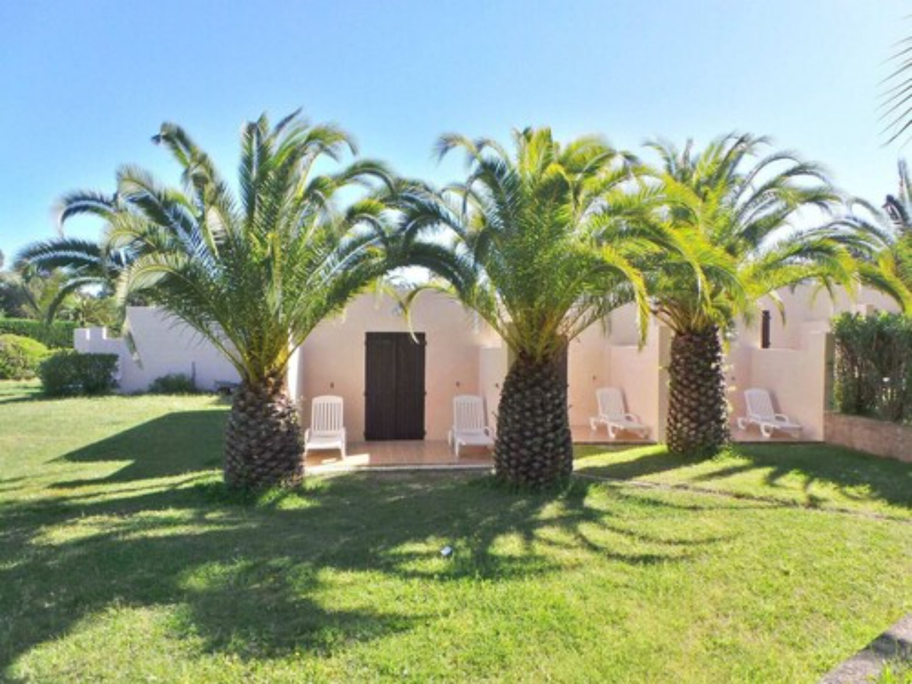 A building with a white exterior, a black door, and a small patio area with white chairs and palm trees.
