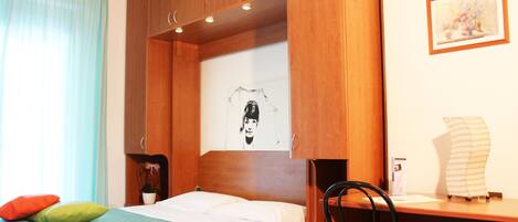 Een hotelkamer met een bed, een bureau, een stoel, een potplant en een schilderij aan de muur.